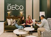 Thumbnail 4 of 42 - Three people are sitting on a green couch in a room with a sign that says "The Deco."