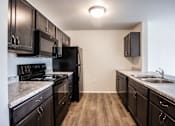 Thumbnail 19 of 21 - A kitchen with black appliances and wooden floors.