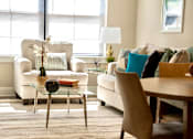 Thumbnail 24 of 50 - A living room with a white sofa, a glass coffee table, and a wooden chair.