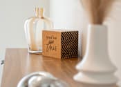 Thumbnail 30 of 50 - A silver object is on a table next to a white vase and a brown card that says "you've got this".