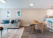 Thumbnail 35 of 50 - A modern living room with a white couch, a glass coffee table, and a dining table with chairs.