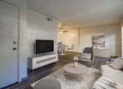 Thumbnail 2 of 13 - A living room with a grey couch, a white coffee table, and a television.
