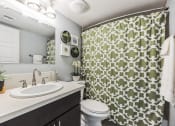 Thumbnail 7 of 23 - a bathroom with a green and white shower curtain and a toilet and sink