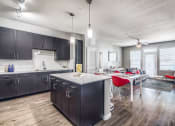 Thumbnail 34 of 37 - a kitchen and living room with dark cabinets and a white table with red chairs at Republic at Alamo Heights, San Antonio, TX