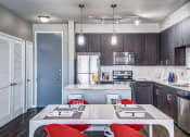 Thumbnail 25 of 37 - a kitchen with dark wood cabinets and white countertops and a white dining table with red chairs at Republic at Alamo Heights, San Antonio, TX 78209