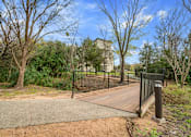 Thumbnail 41 of 72 - a bridge over a creek in a park with trees and a building in the background at Radius on Grove, Austin, TX