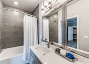 Thumbnail 5 of 36 - A modern bathroom with a white tub, sink, and grey tiled walls at Rosemary Apartments, Conroe, TX, 77384