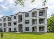 Thumbnail 15 of 36 - A large white apartment building with multiple balconies and a green lawn in front at Rosemary Apartments, Conroe, Texas