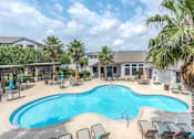 Thumbnail 3 of 36 - A large outdoor swimming pool surrounded by lounge chairs and palm trees at Rosemary Apartments, Conroe, TX, 77384