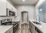 Thumbnail 20 of 36 - A kitchen with a stove, microwave, and sink at Rosemary Apartments, Conroe, Texas