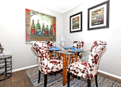 Thumbnail 4 of 16 - A dining room with a glass table and chairs with a wine bottle painting on the wall.