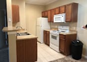 Thumbnail 36 of 36 - A kitchen with white appliances and brown cabinets at Rosemary Apartments, Conroe, TX