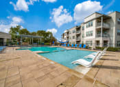 Thumbnail 6 of 27 - a swimming pool with chaise lounge chairs and a slide in front of an apartment building at The Landings at Brooks City-Base, Texas, 78235