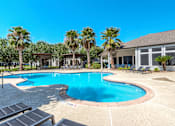 Thumbnail 24 of 36 - A swimming pool surrounded by palm trees and lounge chairs at Rosemary Apartments, Conroe, Texas