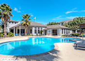 Thumbnail 32 of 36 - A large swimming pool surrounded by palm trees and lounge chairs at Rosemary Apartments, Conroe