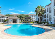Thumbnail 29 of 36 - A large swimming pool in a residential area surrounded by palm trees at Rosemary Apartments, Conroe, TX