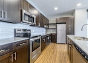 Thumbnail 17 of 25 - a kitchen with wood cabinets and stainless steel appliances at The Fitzroy San Marcos, Texas