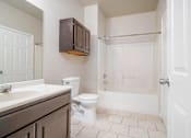 Thumbnail 14 of 35 - Bathroom with tub and wood cabinets at Houston Street Townhomes Apartments, San Antonio, TX