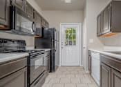 Thumbnail 33 of 35 - Galley kitchen with dark wood cabinets and black appliances at Houston Street Townhomes Apartments, Texas, 78220