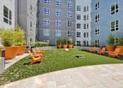 Thumbnail 6 of 12 - A courtyard with orange chairs and a white bench.