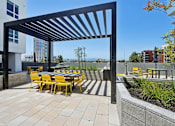 Thumbnail 7 of 12 - A patio with a table and chairs under a black pergola.