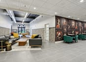 Thumbnail 6 of 26 - A modern living room with a grey sofa, a coffee table, and a large painting on the wall.