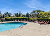 Thumbnail 35 of 46 - A pool surrounded by red lounge chairs and green trees at Island Club Apartments, Ohio