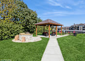 Thumbnail 29 of 46 - A gazebo is situated in a grassy area with a stone wall and a concrete walkway at Island Club Apartments, Ohio, 43235