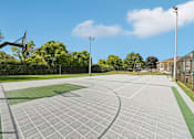 Thumbnail 19 of 24 - A basketball court with a green and grey surface and a basketball hoop on the left side.