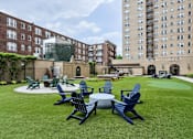 Thumbnail 15 of 26 - A lawn with chairs and tables is surrounded by buildings.