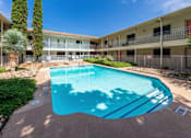 Thumbnail 13 of 13 - A swimming pool in front of a building with trees and bushes around it.