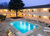 Thumbnail 1 of 13 - A swimming pool surrounded by white lounge chairs and a tree.