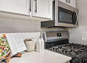 Thumbnail 8 of 30 - A modern kitchen with a stove, microwave, and white cabinets.