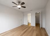 Thumbnail 33 of 35 - A room with a ceiling fan and wooden floors.
