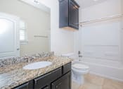 Thumbnail 14 of 22 - A bathroom with a granite countertop and white fixtures at Logan Ridge Apartments, San Marcos