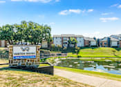 Thumbnail 3 of 42 - A sign for Water Ridge sits in front of a pond and houses at Water Ridge Apartments , Irving, TX