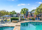 Thumbnail 16 of 42 - A swimming pool surrounded by lounge chairs and umbrellas with a building in the background at Water Ridge Apartments , Irving, TX