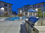 Thumbnail 20 of 22 - a grilling station next to a swimming pool with an apartment building in the background at The Grand at Stonecreek, San Marcos, TX, 78666