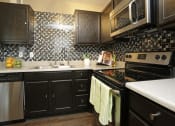 Thumbnail 18 of 55 - a kitchen with black cabinets and a stove and a sink at Water Ridge Apartments, Irving