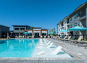 Thumbnail 5 of 52 - A swimming pool with lounge chairs and umbrellas in front of a building at The Virginia Apartments , Texas
