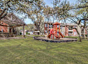 Thumbnail 34 of 42 - A playground with a red swing set is surrounded by trees and a building in the background.