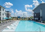 Thumbnail 4 of 52 - A large swimming pool with lounge chairs and umbrellas in front of a building at The Virginia Apartments , Seguin, TX, 78155