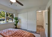 Thumbnail 11 of 23 - A bedroom with a bed, a ceiling fan, and a window with a view of trees.