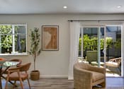 Thumbnail 15 of 23 - A living room with a glass table and chairs, a potted plant, and a framed artwork on the wall.