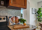 Thumbnail 11 of 39 - A kitchen with a black stove top oven and a cutting board with an orange on it.
