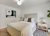 Thumbnail 17 of 27 - A bedroom with a bed, nightstand, and a painting on the wall.
