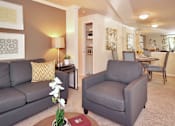 Thumbnail 10 of 18 - A grey sofa and armchair in a living room with a table and a vase of flowers.