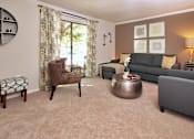 Thumbnail 15 of 18 - A living room with a grey couch, a brown chair, a round coffee table, and a small potted plant on a side table.