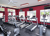 Thumbnail 14 of 18 - A gym with treadmills, elliptical machines, and a fan.