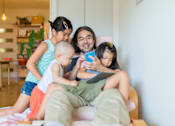 Thumbnail 5 of 18 - A man is reading a book to two children on a couch.